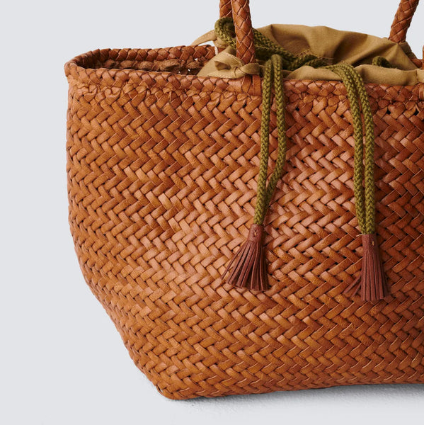 Woven brown bag with green drawstring and tassels on a light gray background