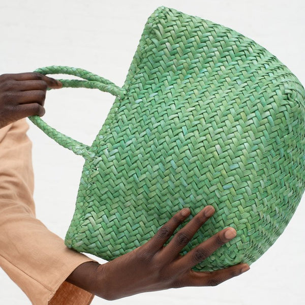 Green woven bag held by a person against a white background
