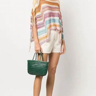 Woman wearing a colorful striped top and white shorts, holding a green bag on a white background