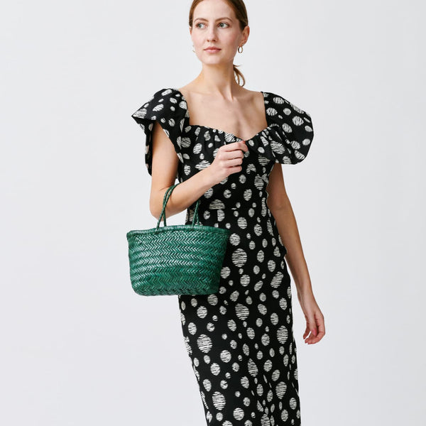 Woman in a black and white polka dot dress holding a green bag on a white background