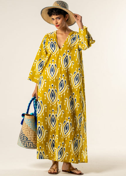 Woman wearing a yellow patterned dress with a straw hat and blue bag on a white background