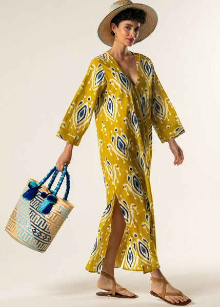 Woman wearing a yellow patterned dress holding a decorative bag on a white background