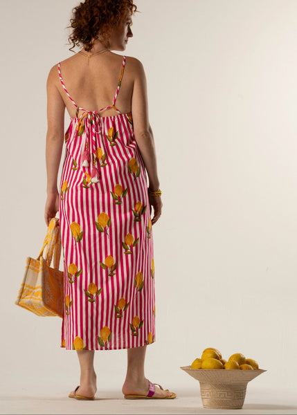 Woman in a red and white striped dress with fruit pattern, holding a yellow bag, standing next to a basket of lemons.
